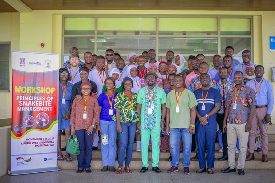 Participants and speakers of the training course on November 7, 2023. The picture shows a group of people standing in front of a hospital entrance next to a banner which says 'Workshop - Principles of Snakebite Mangement'. Everyone is looking friendly into the camera.