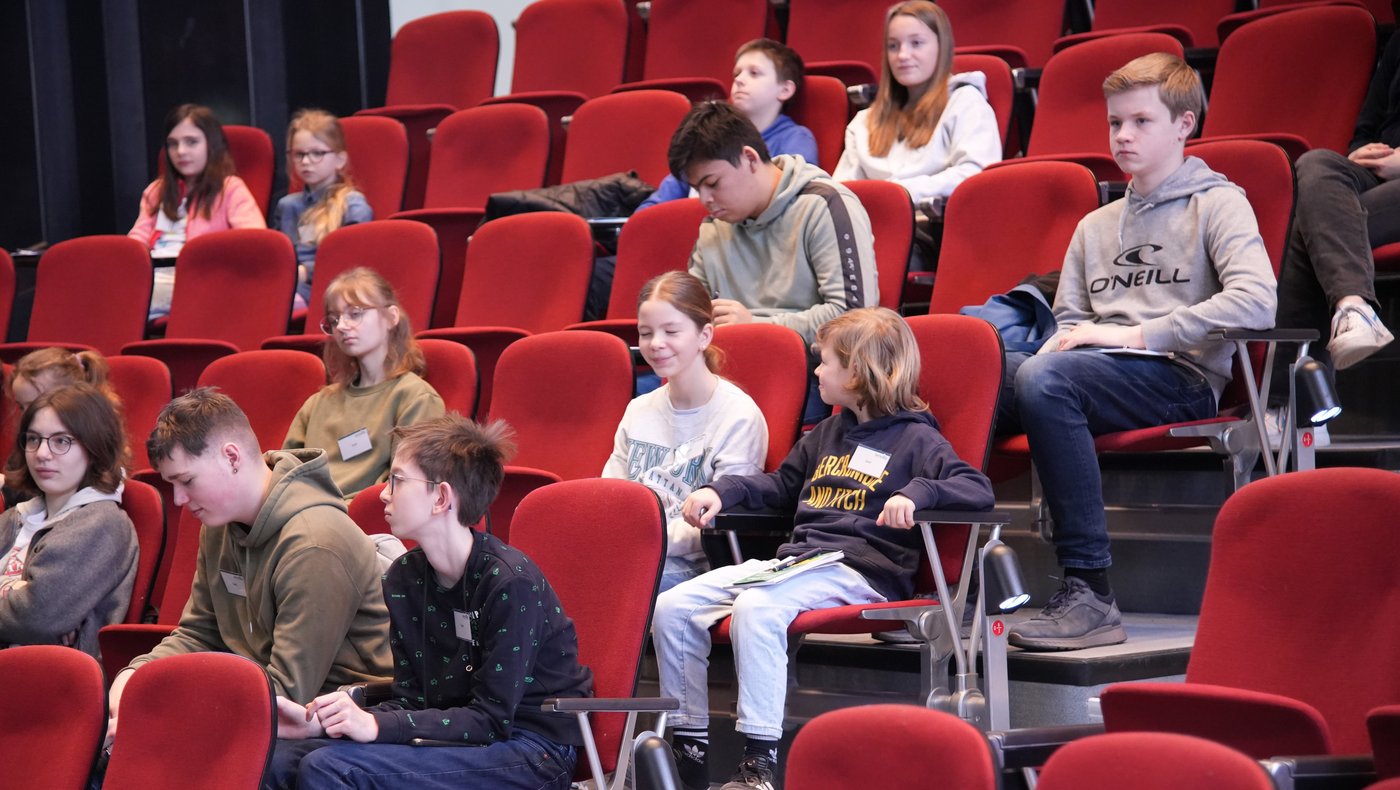 Das Foto zeigt mehrere Kinder auf den rot gepolsterten Sitzen im historischen Hörsaal.