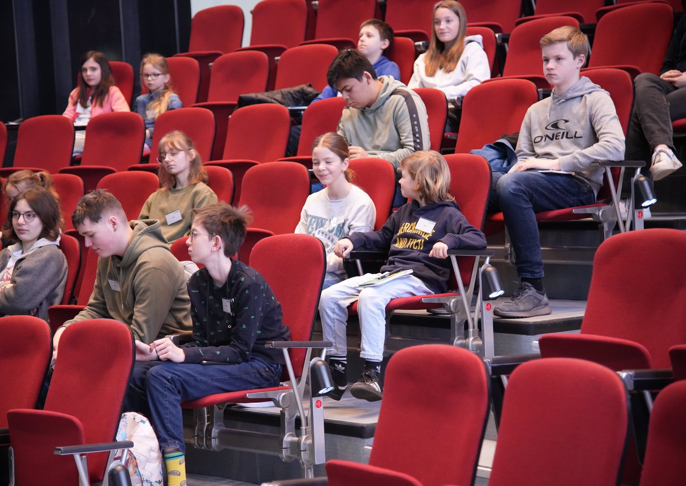 Das Foto zeigt mehrere Kinder auf den rot gepolsterten Sitzen im historischen Hörsaal.