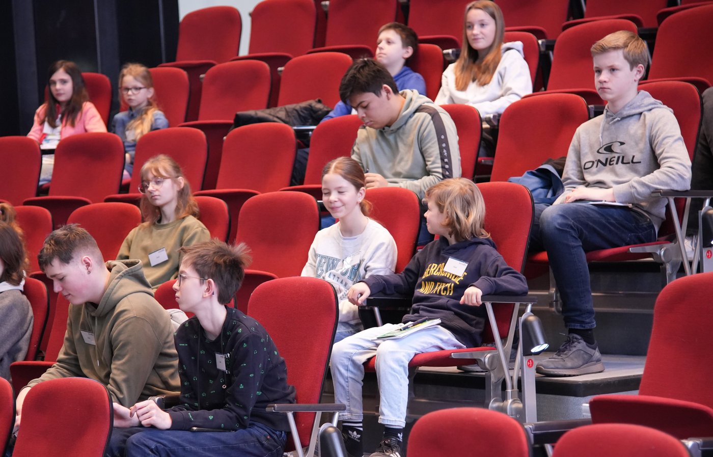 Das Foto zeigt mehrere Kinder auf den rot gepolsterten Sitzen im historischen Hörsaal.