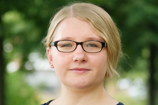 Dr. Lisa Oestereich Dr. Lisa Oestereich: eine Forscherin mit brauner Brille, blonden Haaren, die zu einem Zopf gebunden sind und blauer Bluse, im Hintergrund grüne Äste.