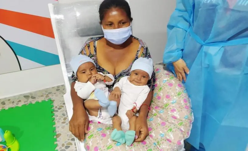Mother is in hospital bed. She holds her two newborn children.
