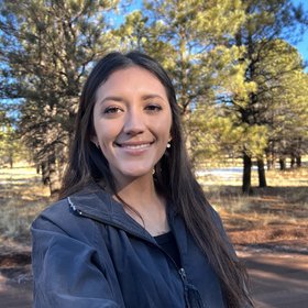 Kandace Baez, a PhD student, is shown standing in front of large cacti in Arizona