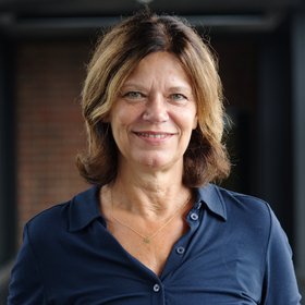 The portrait photo shows a researcher with shoulder-length brown hair, wearing a dark blue blouse.