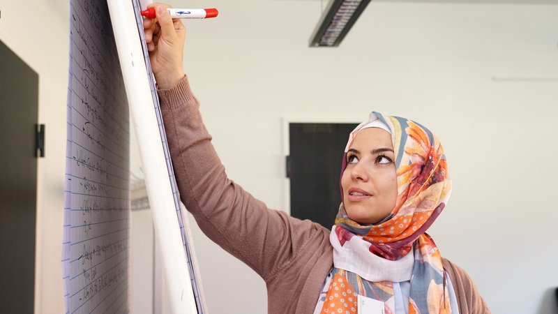 Eine Wissenschaftlerin mit einem Kopftuch schreibt konzentriert Notizen an ein Flipchart.