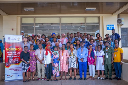 Participants and speakers of the training course on November 8, 2023. The picture shows a group of people standing in front of a hospital entrance next to a banner saying 'Workshop - Principles of Snakebite Management'. Everyone is looking friendly into the camera.