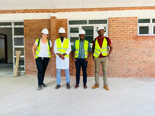 From left to right: Dr. Friederike Hunstig (BNITM), Dr. George Limwado (Partners in Health), Dr. Albert Chafunya (Neno District Health Office), Moses Aron (Partners in Health/BNITM) on a tour of the construction site of the new emergency room at Lisungwi The picture shows four people wearing high-visibility vests and safety helmets in front of a building. They are all smiling at the camera.