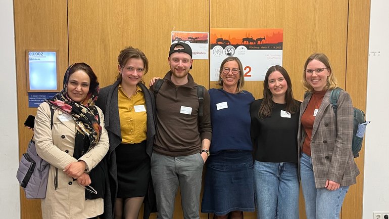 Strongyloides meeting Eine gemischte Gruppe von Menschen steht zusammen vor einer strukturierten Wand, lächelt und unterhält sich miteinander.