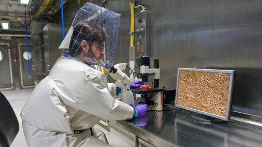 Zu sehen ist eine Person im Hochsicherheitsanzug bei der Arbeit in einem Sicherheitslabor der Risikostufe 4.