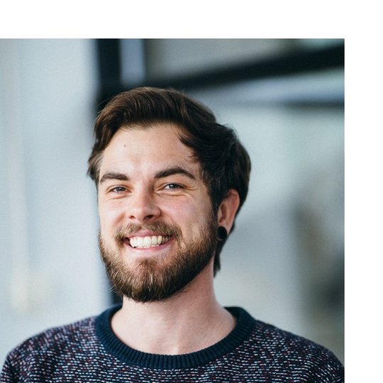 Erik Tove Zillmann Portrait of a white male bearded person, wearing a blue-red-white sweater, smiling into the camera.