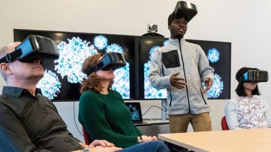 Simulation of scenarios using 3D technology Several people wearing VR glasses. A man with his glasses pushed up talks to the group.