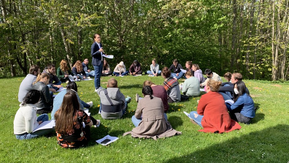 LCI Summer School Eine Wissenschaftlerin steht auf dem Rasen im Kreis weiterer Teilnehmer:innen der LCI Summer School und hält einen Vortrag.