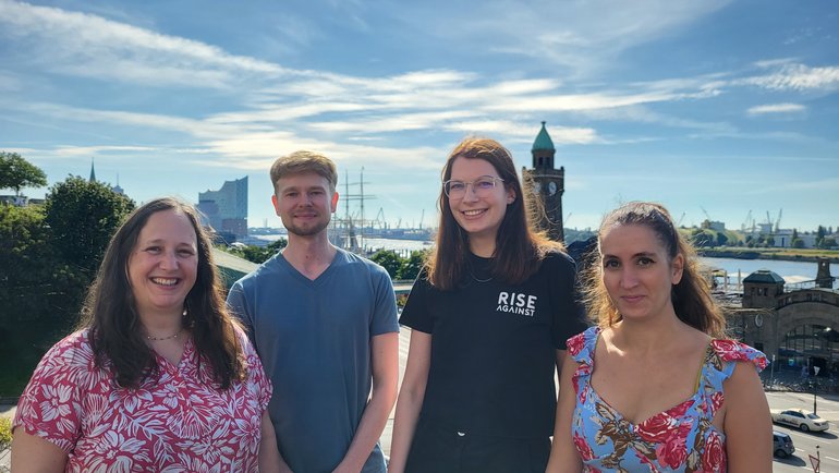 Research Group Escudero-Pérez Gruppenfoto Laborgruppe Escudero-Pérez: 4 Personen stehen draußen vor blauem, mit leichten Schleierwolken bedecktem Himmel und tragen sommerliche Kleidung.