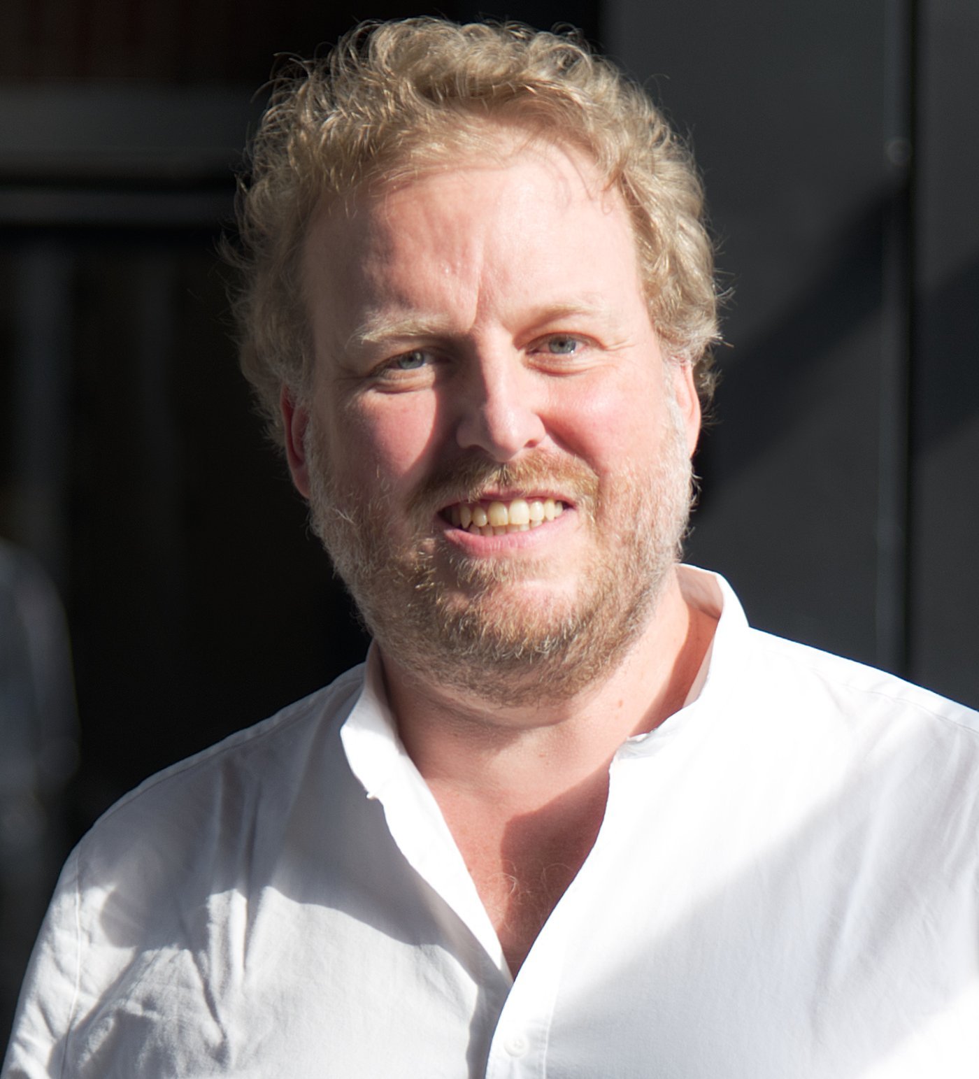 Dr. Florian Gehre Das Foto zeigt Dr. Florian Gehre. Er trägt kurze rötliche Locken, einen Dreitagebart und ein weißes Hemd und lächelt freundliche in die Kamera.