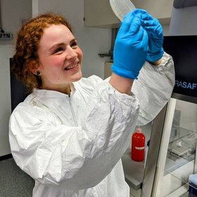 Anna-Lena Schmitz, a researcher in a lab coat holds a white object, symbolizing scientific inquiry and innovation in a laboratory setting.