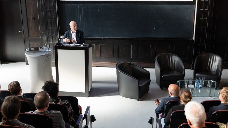 Hamburgs Erster Bürgermeister Dr. Peter Tschentscher Foto des Ersten Bürgermeisters Dr. Peter Tschentscher am Redepult im historischen Hörsaal des BNITM. Im Vordergrun dicht besetzte Sitzreihen.