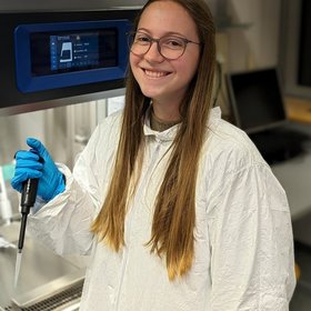 Joelle van der Ham, a researcher with blond hair, holds a thermometer while wearing a lab coat in a laboratory setting