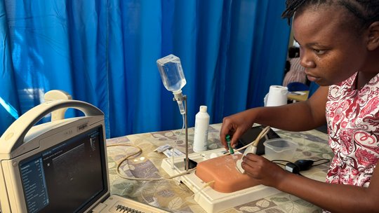 Training with intervention models during the POCUS training. The picture shows a woman using a point of care ultrasound on a model while looking at a monitor.