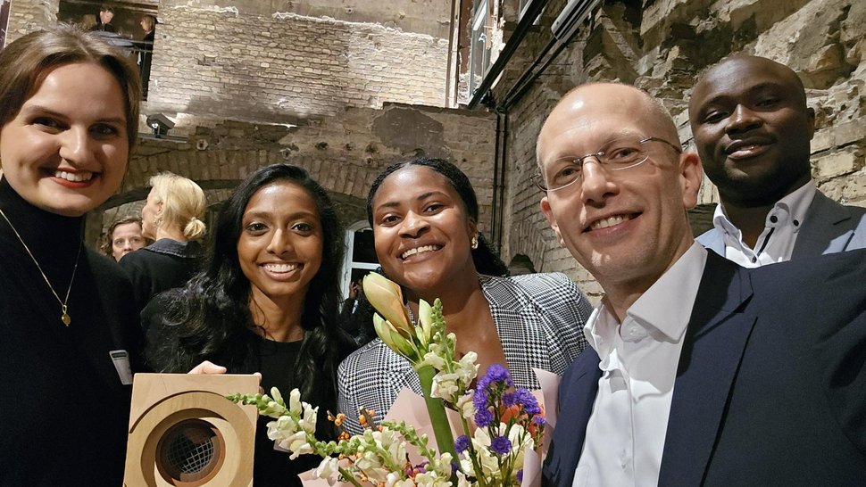 Das Foto zeigt eine diverse Gruppe nach der Preisverleiung mit Blumen und rechteckigem Preis in der Hand.