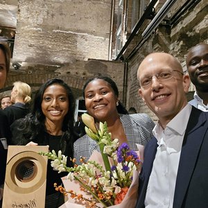 Das Foto zeigt eine diverse Gruppe nach der Preisverleiung mit Blumen und rechteckigem Preis in der Hand.