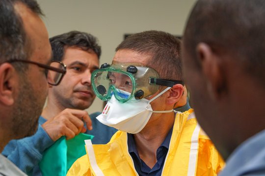 Putting on the personal protective equipment (PPE). The picture shows several men helping a colleague dress in a personal protective equipment (PPE).