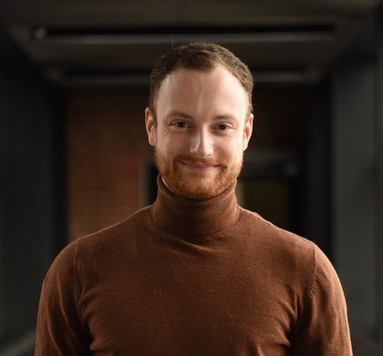 Dr. Lennart Heepmann Dr. Lennart Heepmann: Ein Doktorand in schwarzem Shirt lächelt in die Kamera. Er trägt kurzes rot-braunes Haar und einen roten dreitage Bart.