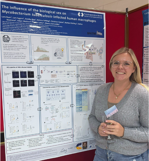Lara Buer presenting her poster Lara Buer stands to the right of her poster and smiles warmly at the camera. She is wearing jeans and a gray pullover.