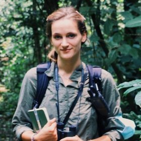 Dr. Elodie Freymann, a researcher, wearing a green shirt and backpack, holds a camera, ready to capture her surroundings during fieldwork.