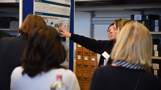 Dr. Sophie Duraffour im Gespräch mit Gutachter:innen Eine Forscherin steht vor einem Poster der Virologie-Abteilung und erklärt einer Gruppe etwas.