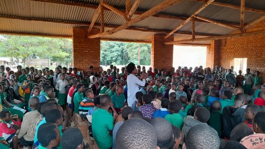 Community engagement - Joseph Tepani during the school visits The picture shows a man standing in a crowd of school children who are looking at him.