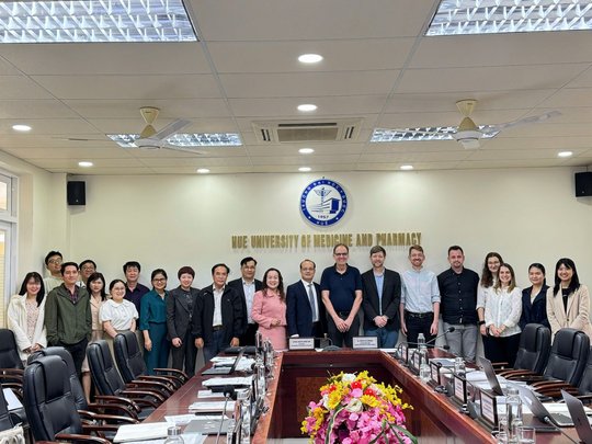 Group picture at the official kick-off meeting. The picture shows several people standing in front of a logo of the Hue University of Medicine and Pharmacy.