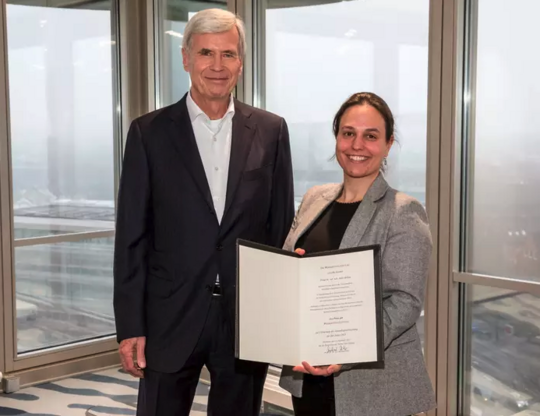 Award of the Werner Otto Prize to BNITM scientist Dr Julie Sellau. Dr. Julie Sellau erhält in einem festlichen Rahmen die Urkunde überreicht. Im Hintergrund sieht man bodentiefe Fenster und einen grauen Wintertag.