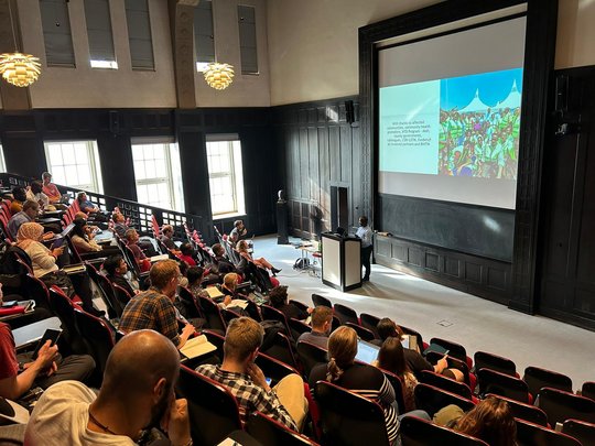 Lecturer during the summer school on snakebite envenoming The picture shows a crowded lecture hall and a lecturer at the podium.