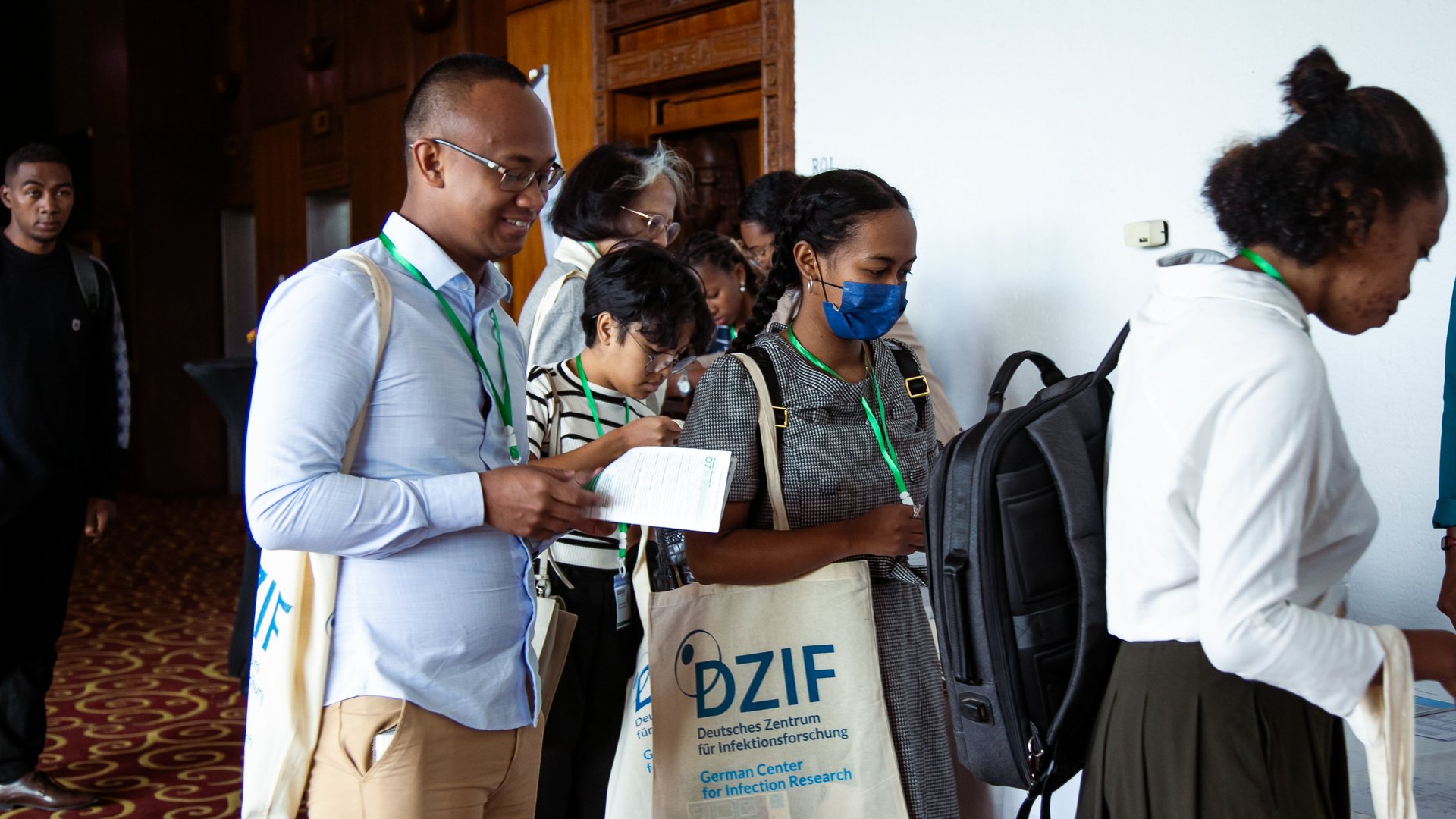 CCSM event staff at a registration table assisting attendees by distributing materials and providing guidance, with tote bags and documents displayed on the table.