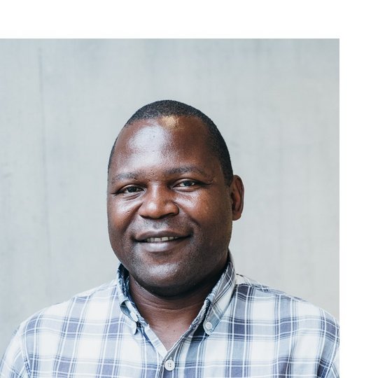 Kennedy Muhindo Wema Portrait of a male Black person wearing a white and blue chequered shirt.