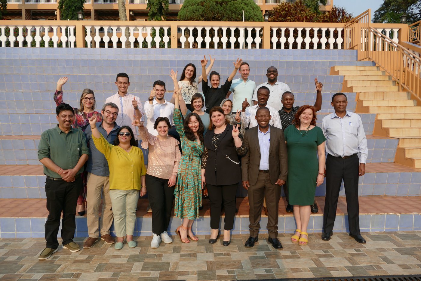 Das Foto zeigt eine Gruppe von Personen in Kampala draußen vor einer großen Treppe, einige winken in die Kamera.