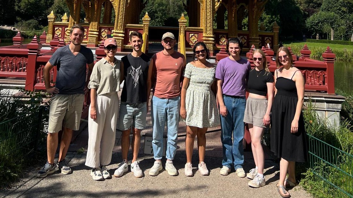 A team of eight scientists stands in front of a pagoda and smiles into the camera