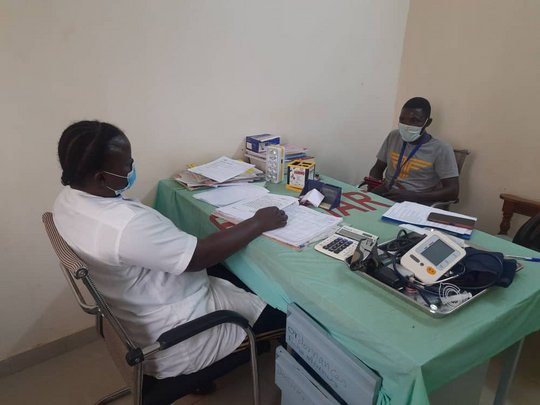 ACHES project Zu sehen ist ein Arzt und ein Patient aus Burkina Faso, die sich gegenüber an einem Tisch mit unterschiedlichen Untersuchungsgeräten und Unterlagen sitzen.