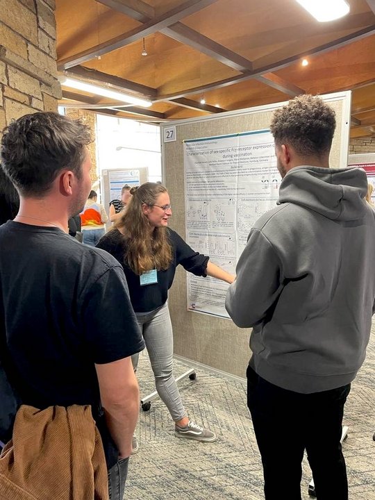 Charlotte Hansen present their latest research results in the poster session of the Gordons Conference. Frau Hansen steht vor ihrem Poster und zeigt zwei interessierten Besuchern ihre Ergebnisse. Sie deutet dabei mit einem Finger auf eine Grafik und gibt den Interessierten Auskunft.