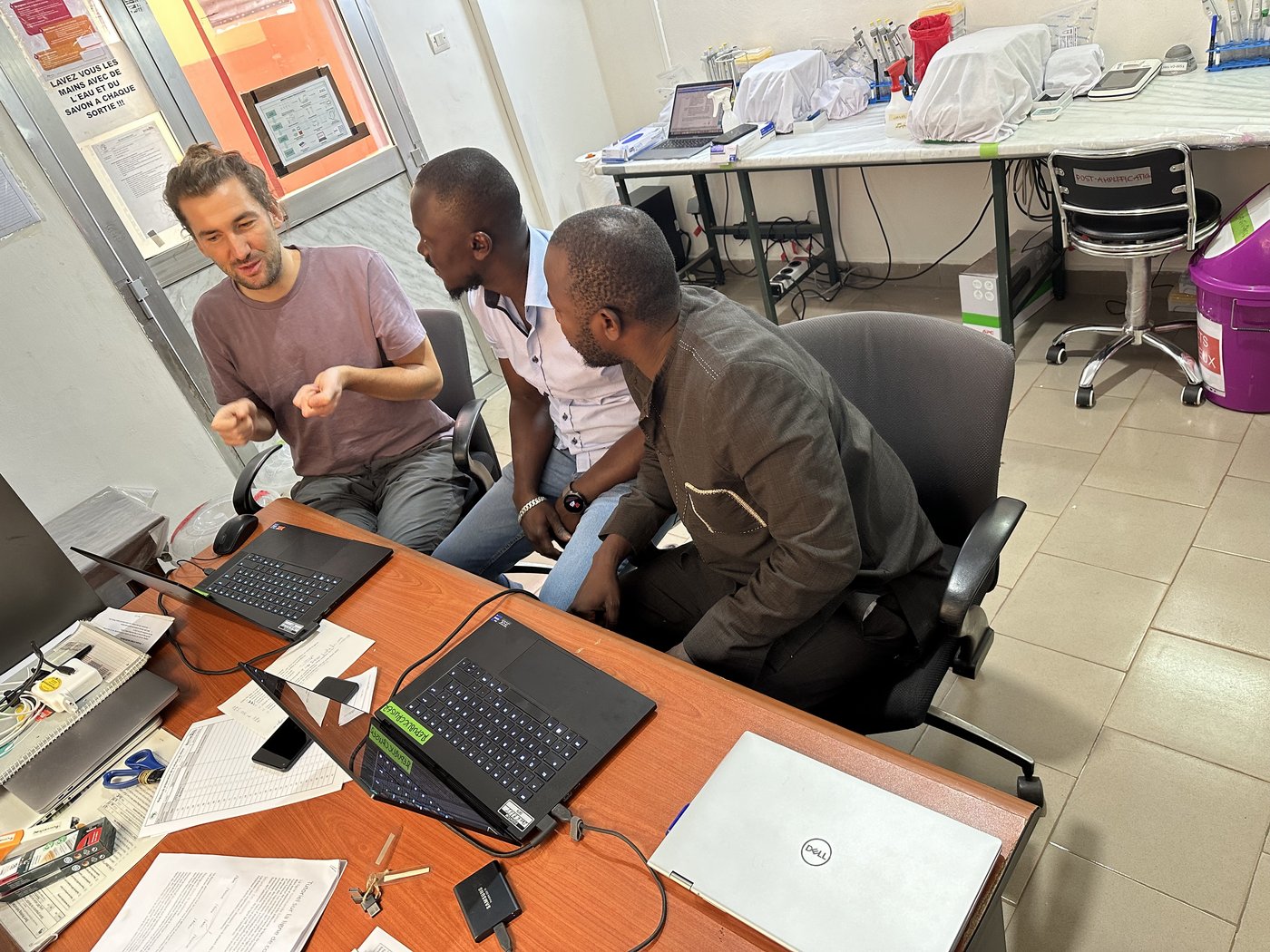 Two laboratory staff discussing with one trainer in front of two laptops used for bioinformatic analysis in the sequencing laboratory.