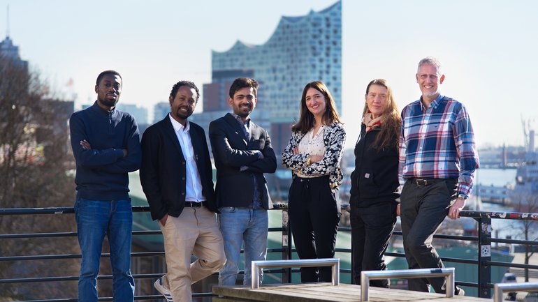 Group photo Research Group One Health Bacteriology An ethnically mixed group of scientists looking friendly into the camera in front of a sunlit harbour