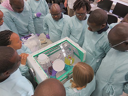 Teaching of Glove-Box Usage Das Bild zeigt verschiedene Forscher, die einer weiteren bei Laborarbeiten zusehen
