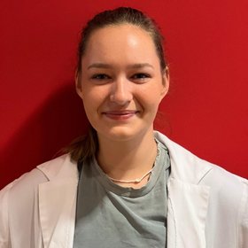 Henrike Wurm, a researcher with brown hair, smiles warmly while wearing a white coat, embodying the spirit of scientific research.