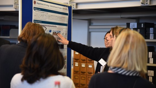 A researcher is standing in front of a poster from the virology department and explaining something to a group.