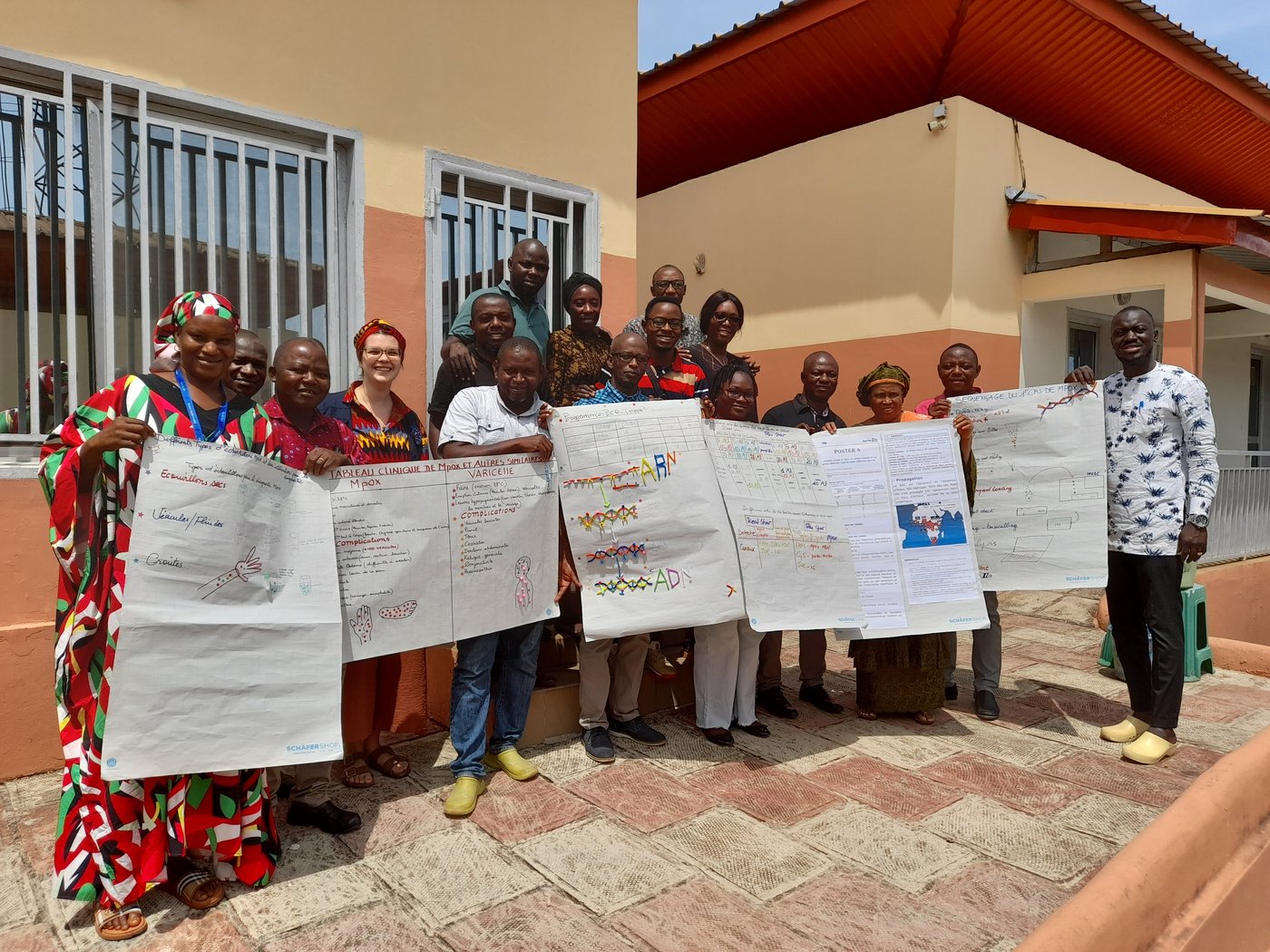 sixteen laboratory staff with one trainer all standing together with posters after training for a group photo