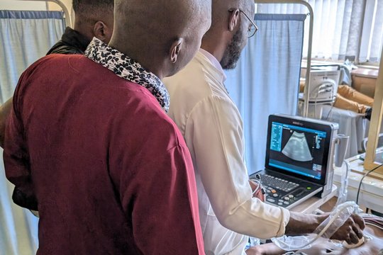 Scanning of volunteers during the POCUS training at the University of Zimbabwe The picture shows three men standing over a volunteer who is being scanned with an ultrasound device.