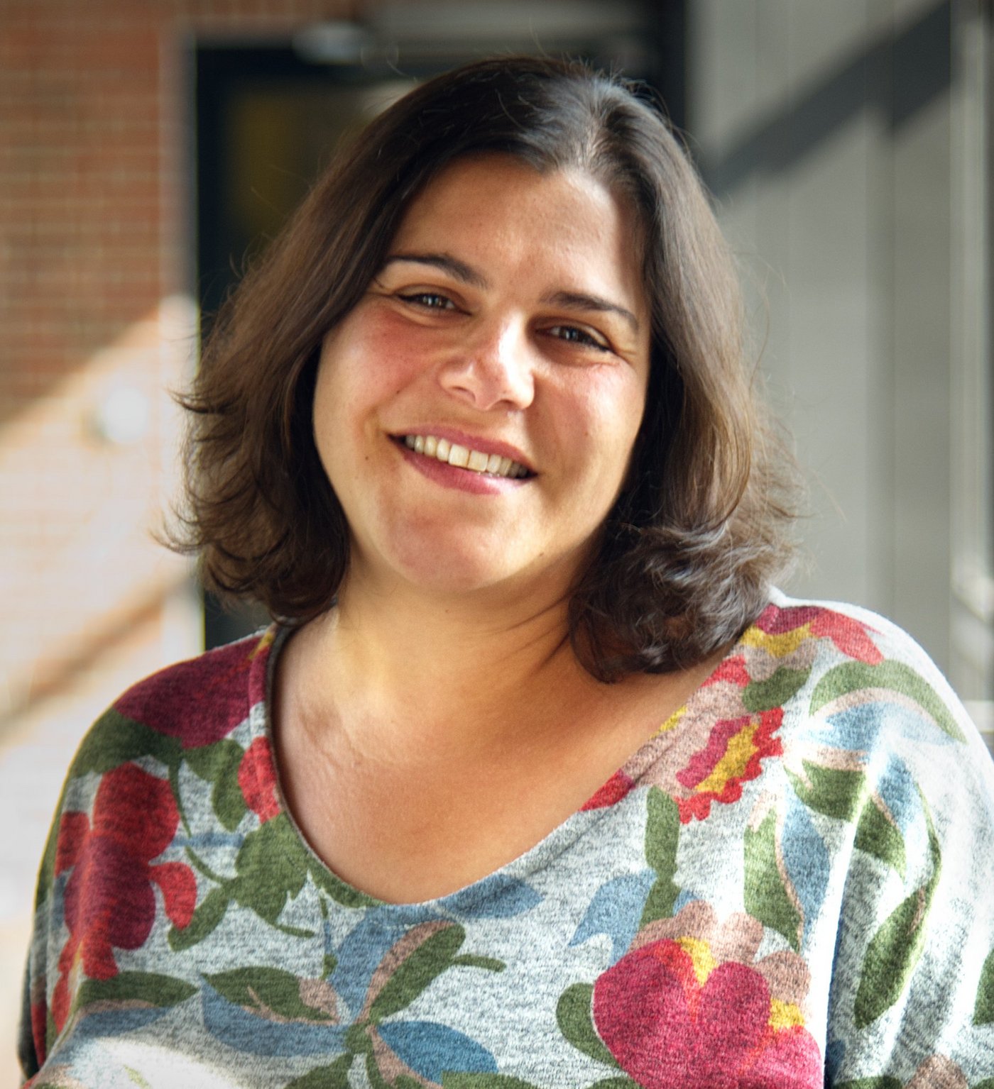 Dr. Muna Affara Das Foto zeigt die Forscherin Muna Affara. Sie trägt halblange dunkle Haare, einen bunten mit großen Blumen bedruckten Pullover und lächelt freundlich in die Kamera.