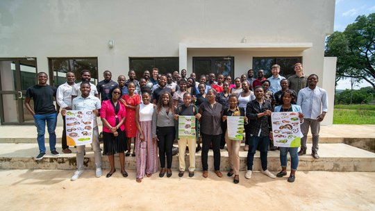 Training participants and lecturers of the training held on 6th of March Das Bild zeigt eine Gruppe an Menschen mit Postern über Schlangen vor einem Gebäude.