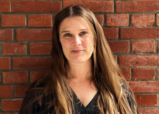 Dr. Anna Bachmann Anna Bachmann: eine Forscherin steht draußen vor einer Backsteinwand und lacht in die Kamera.