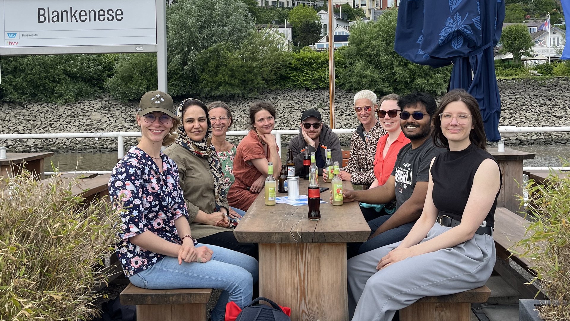 Group outing at river Elber A group of smiling people sitting around a table outdoors next to a sign saying "Blankenese"